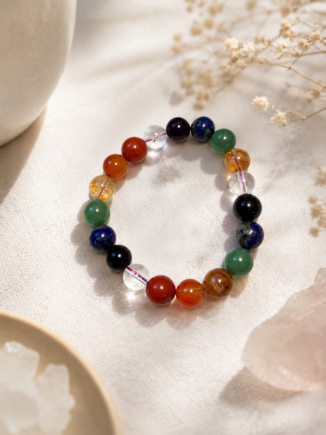 7 Chakra Bracelet styled on linen with dried flowers and a rose quartz crystal, seven chakra stones visible