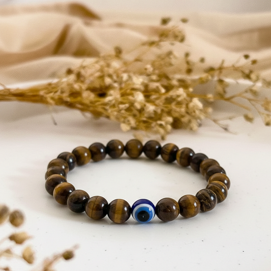 Beaded bracelet with a blue evil eye bead on a white surface with dried flowers.