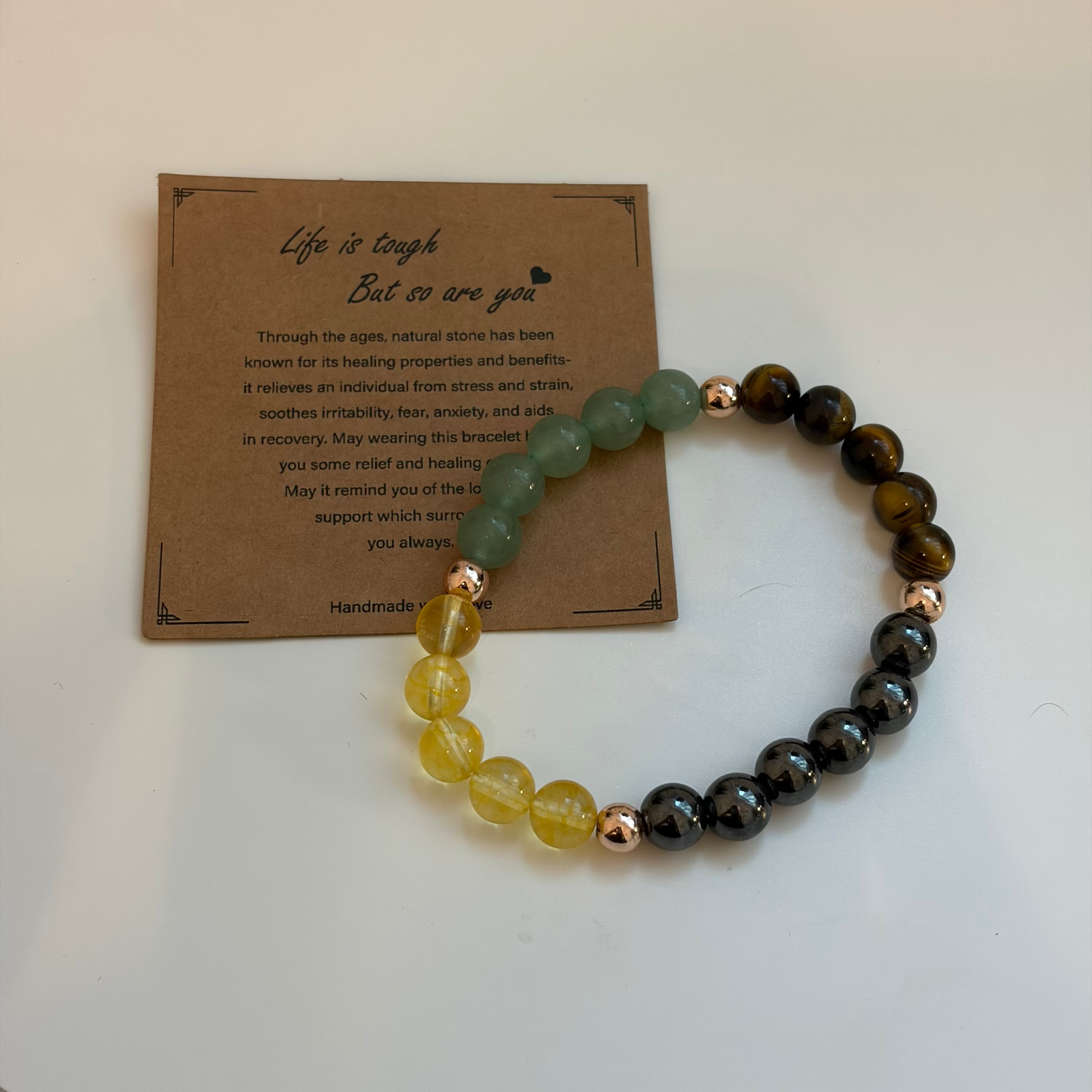 Bracelet with multicolored beads on a white surface next to a motivational card.