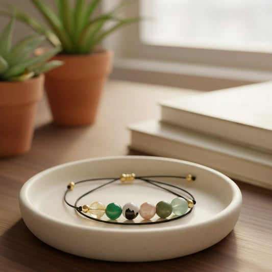 White ceramic dish with a bracelet featuring green stones on a wooden surface with plants and books in the background.