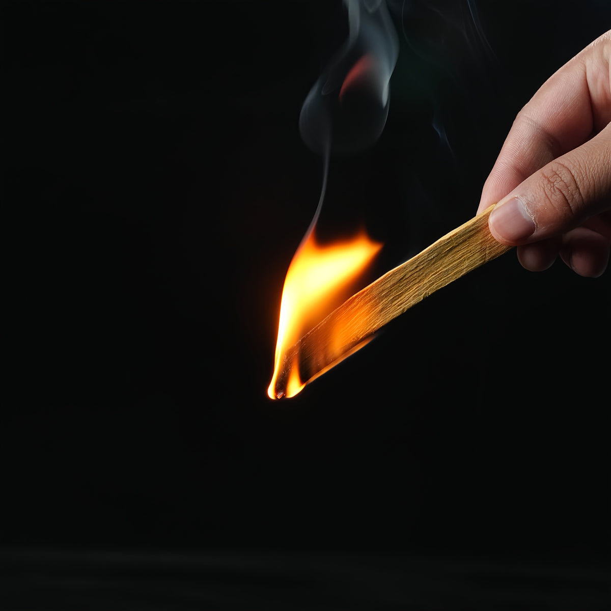 A hand lighting a palo santo stick, flame catching the end of the sacred wood