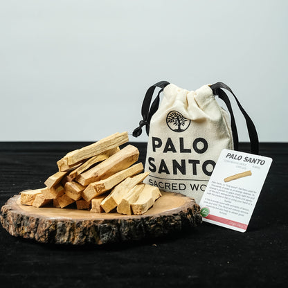 Palo santo sticks stacked on a wooden slice beside the Sacred Wood pouch and card